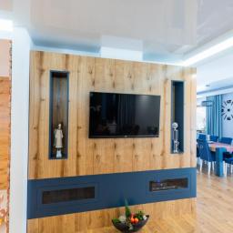 GERLEJ Gerard Lejk - Drewniana ściana telewizyjna na wymiar z wnękami na dekoracje i niebieskim panelem dolnym, z widoczną częścią jadalni w tle.