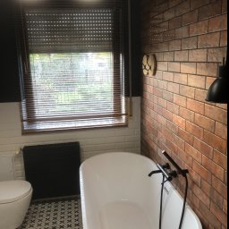 ART-DOM Tomasz Frankiewicz - Nowoczesna łazienka z wolnostojącą białą wanną, czarną armaturą i grzejnikiem, ceglaną ścianą z dekoracyjnymi wieszakami, wzorzystą podłogą i oknem z żaluzjami.