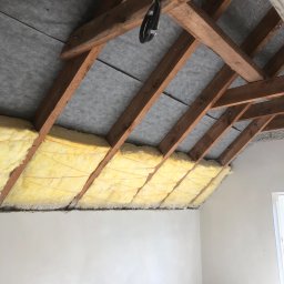 ART-DOM Tomasz Frankiewicz - Konstrukcja drewniana poddasza z izolacją z wełny mineralnej, zabezpieczona szarą membraną, widoczne przewody elektryczne w peszlu.