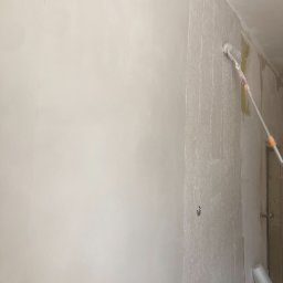 ART-DOM Tomasz Frankiewicz - Malowanie ścian wałkiem teleskopowym na biało, widoczne puszki instalacyjne i częściowo pomalowana ściana.