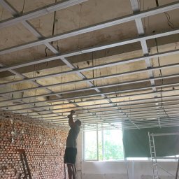 ART-DOM Tomasz Frankiewicz - Montaż metalowej konstrukcji sufitu podwieszanego w surowym wnętrzu z odsłoniętą cegłą i laserowym niwelatorem.