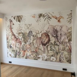ART-DOM Tomasz Frankiewicz - Fototapeta w pokoju dziecięcym z motywem dżungli i zwierząt, takich jak żyrafa, lew, słoń i zebra, wykończona białą listwą przypodłogową.