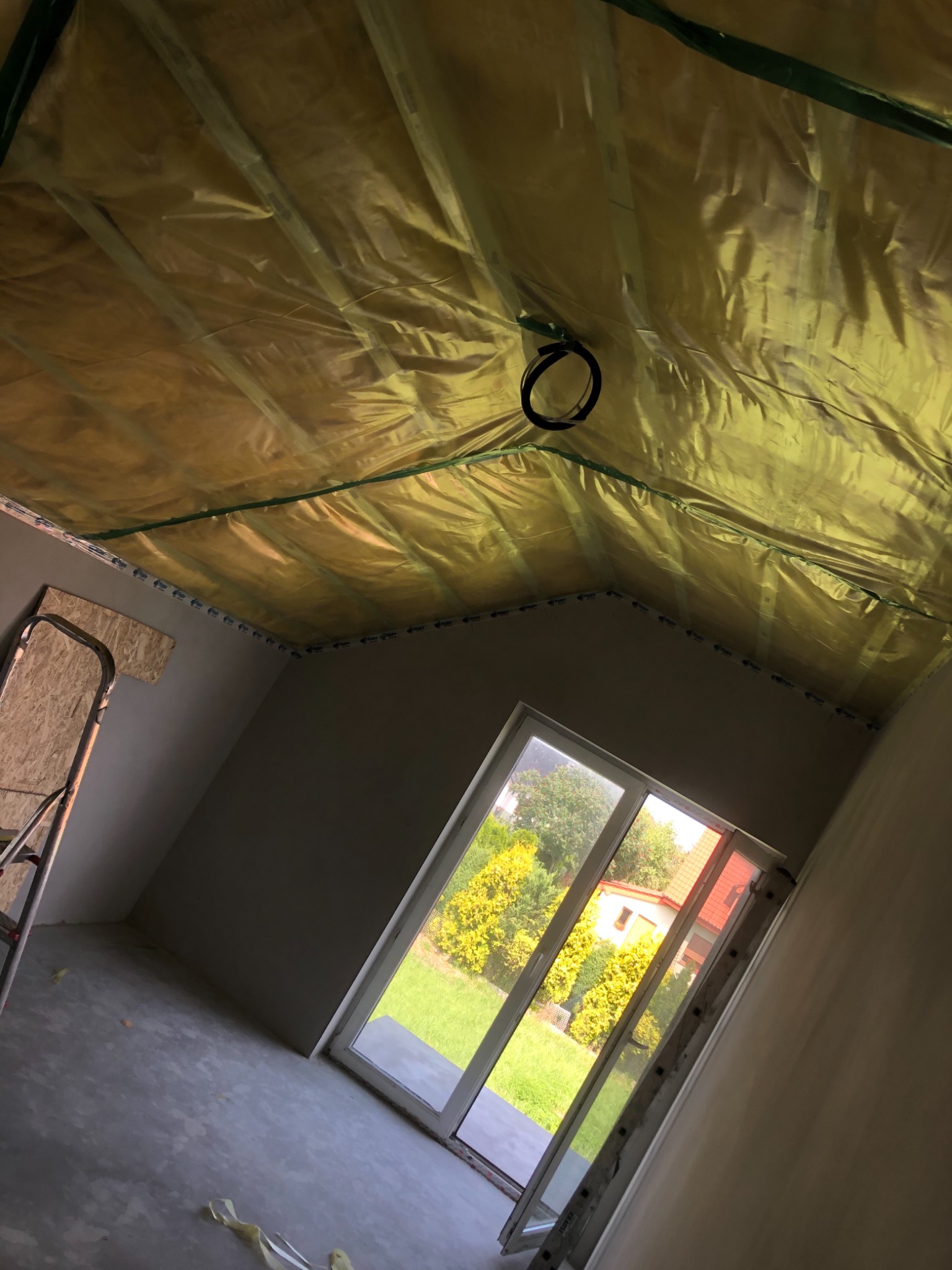 Przygotowanie do montażu sufitu: folia paroizolacyjna zamontowana na konstrukcji drewnianej poddasza, widoczne okablowanie i drabina w pomieszczeniu z oknem.