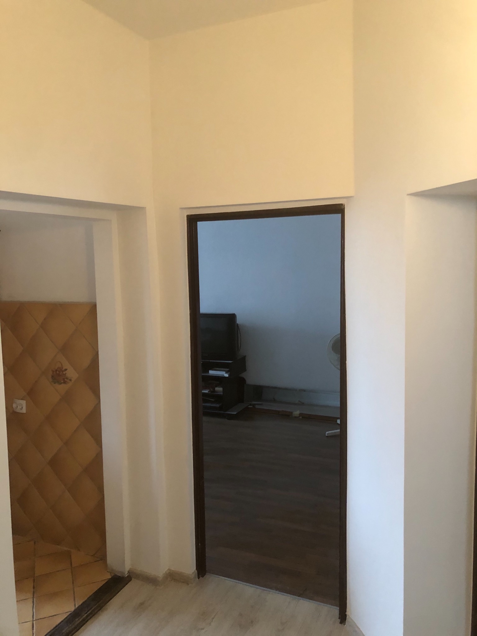 Wnętrze mieszkania po remoncie, widok na odnowioną łazienkę z beżowymi płytkami w romby i zamontowane, ciemne, przeszklone drzwi do pokoju z ciemną podłogą.