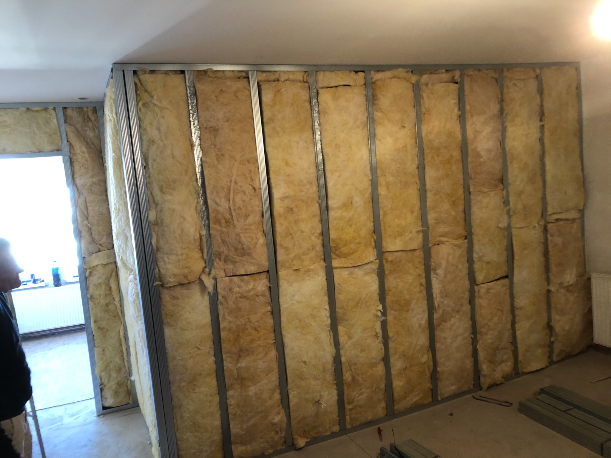 Montaż ścianki działowej: metalowy stelaż wypełniony wełną mineralną, widoczne profile i izolacja przed płytami gipsowo-kartonowymi.