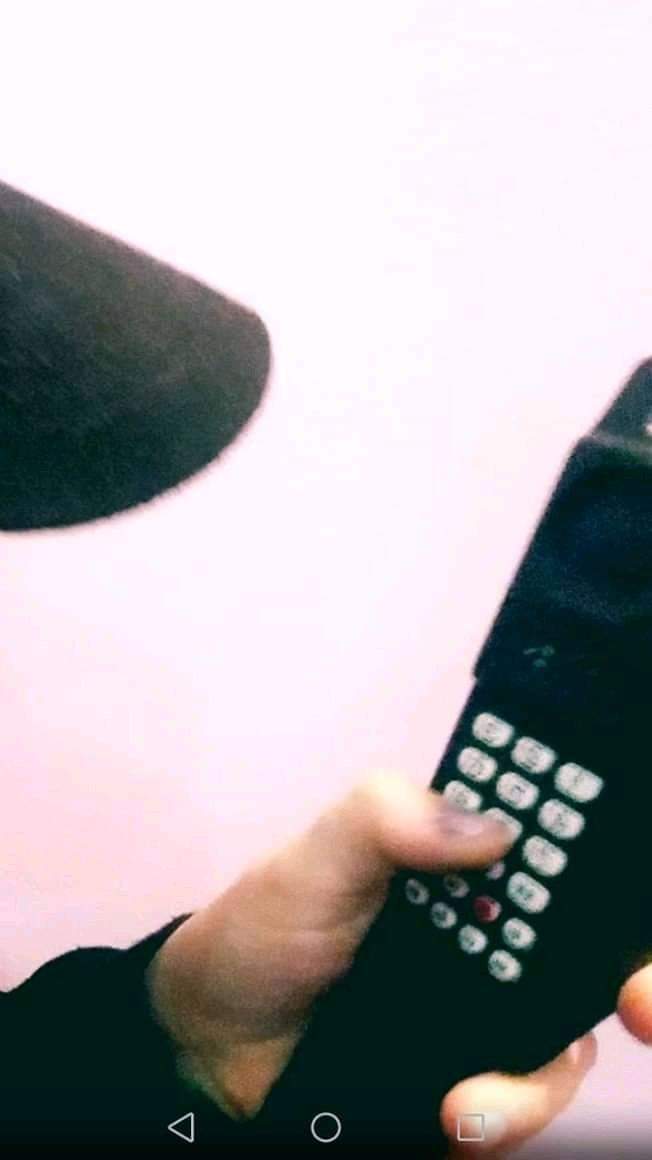 Dłoń naciska przyciski na czarnym telefonie komórkowym z anteną, widoczny fragment mikrofonu i różowe tło.