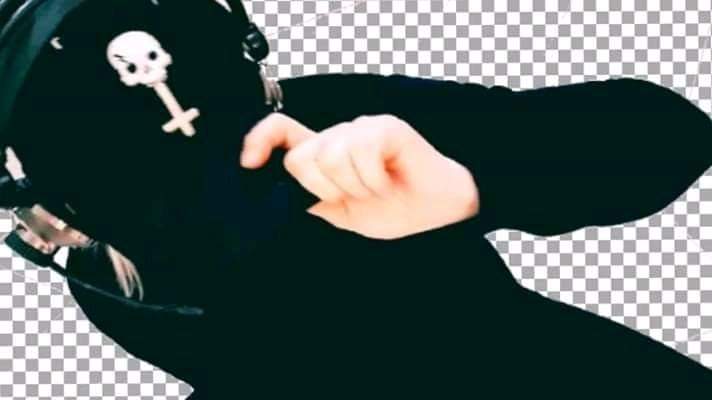 Osoba w czarnym stroju z kapturem i słuchawkami, na której widnieje biała czaszka z krzyżem, zasłaniająca twarz ręką na tle szachownicy.