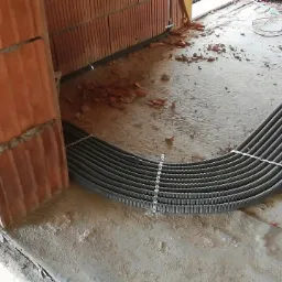 Instalacja elektryczna w peszlach prowadzona wzdłuż ściany z czerwonej cegły dziurawki na surowym betonowym podłożu w trakcie budowy domu.