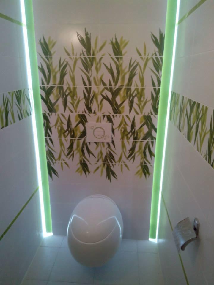 Nowoczesna toaleta z podświetleniem LED i dekoracyjnymi płytkami z motywem roślinnym.