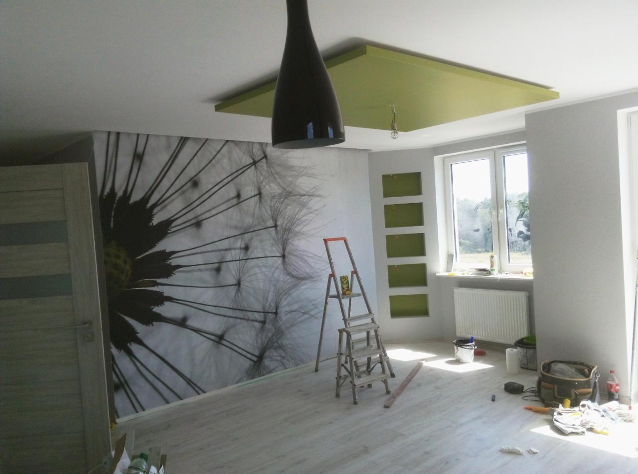 Pokój po odświeżeniu z fototapetą dmuchawca na ścianie, zielonym podwieszanym sufitem i wnękami, drabina malarska w centrum, narzędzia i akcesoria malarskie na podłodze.