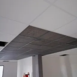 Montaż sufitu podwieszanego z widoczną konstrukcją rusztową i częściowo zamontowanymi panelami akustycznymi, drabina malarska w tle.