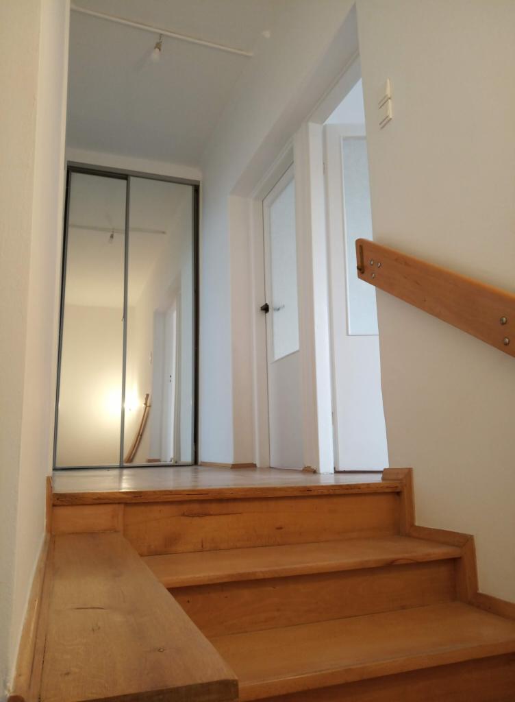 Drewniane schody prowadzące do przedpokoju z szafą wnękową z lustrzanymi drzwiami i białymi drzwiami po prawej stronie, widok z dołu.