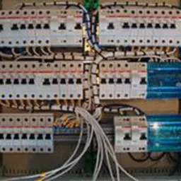 Otwarta skrzynka elektryczna z licznymi bezpiecznikami i okablowaniem wewnątrz, widok z góry.