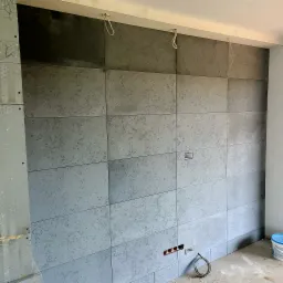 Montaż betonowych płyt architektonicznych na ścianie, widoczne puszki elektryczne i przewody, surowy stan wykończenia.