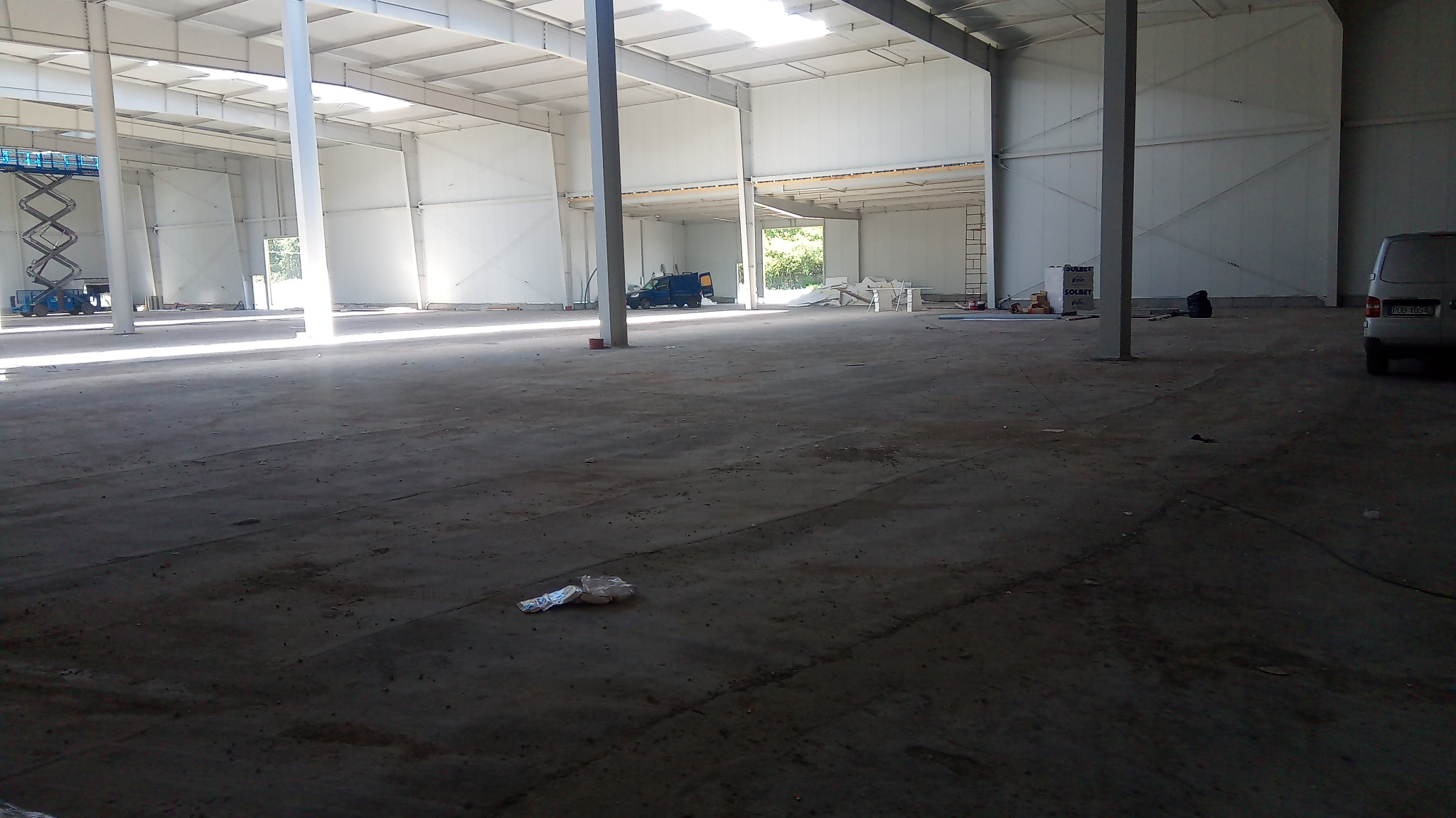 Przygotowanie do wylania posadzki w hali przemysłowej: widoczna surowa powierzchnia, sprzęt budowlany w tle i częściowo oświetlona przestrzeń.