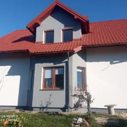 Nowo wybudowany dom jednorodzinny z czerwoną dachówką i szarymi ścianami, widok z zewnątrz w słoneczny dzień.