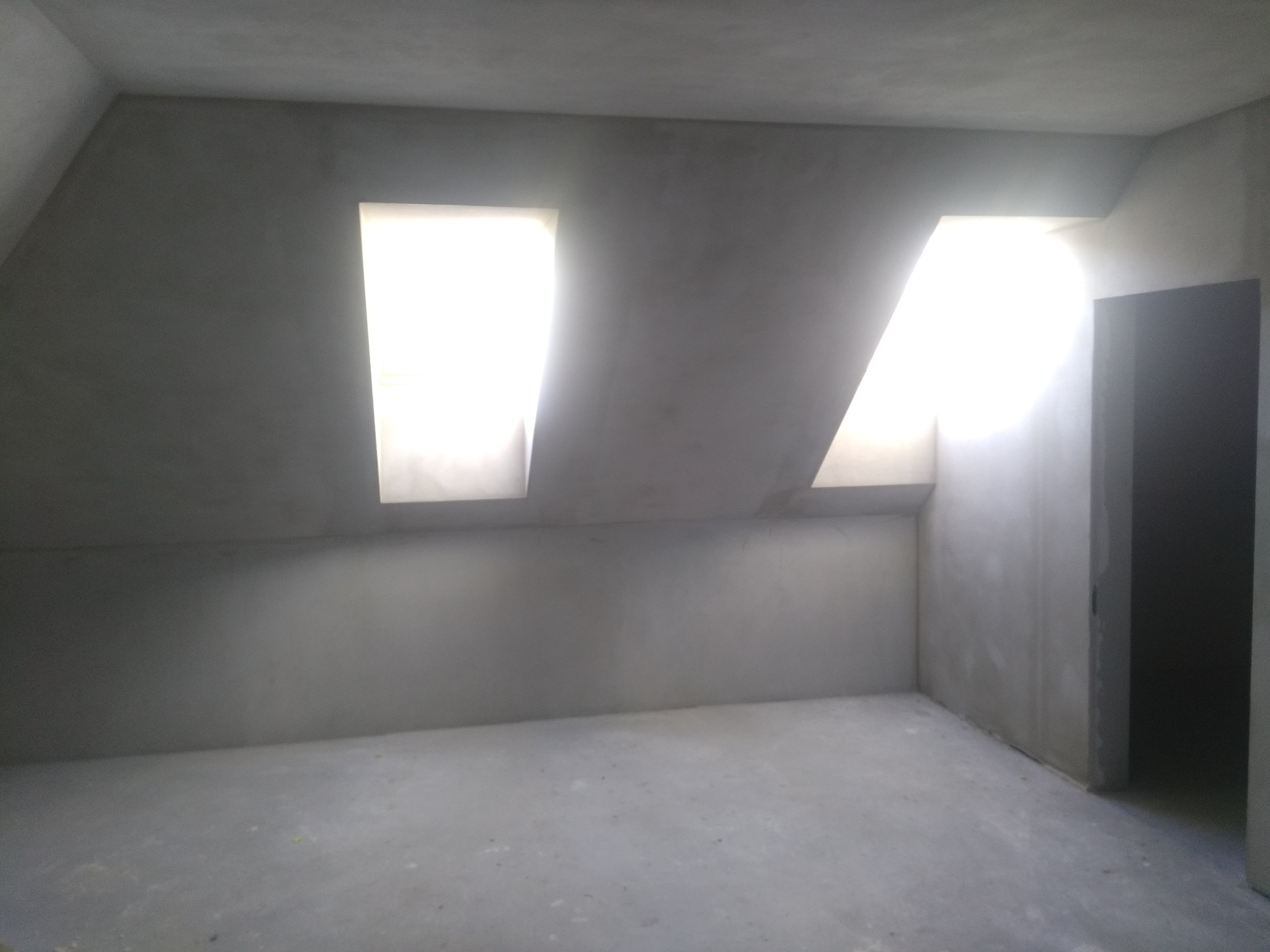 Poddasze po szpachlowaniu, z dwoma oknami dachowymi w skosach, widoczne ślady po łatach na ścianach, przygotowane do dalszych prac wykończeniowych.