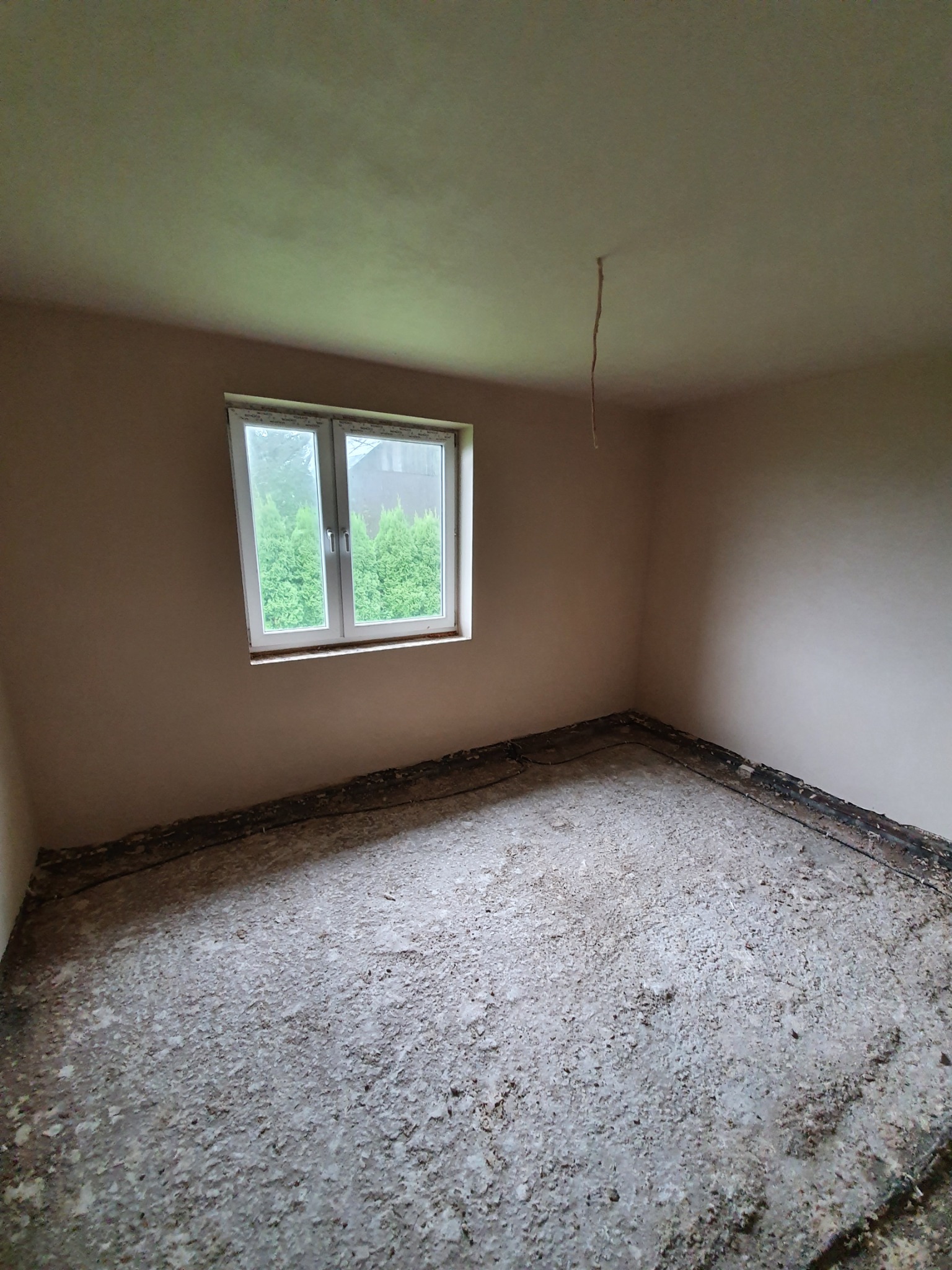 Pokój po nałożeniu tynków maszynowych, widoczne niedoskonałości posadzki i wystający kabel z sufitu.