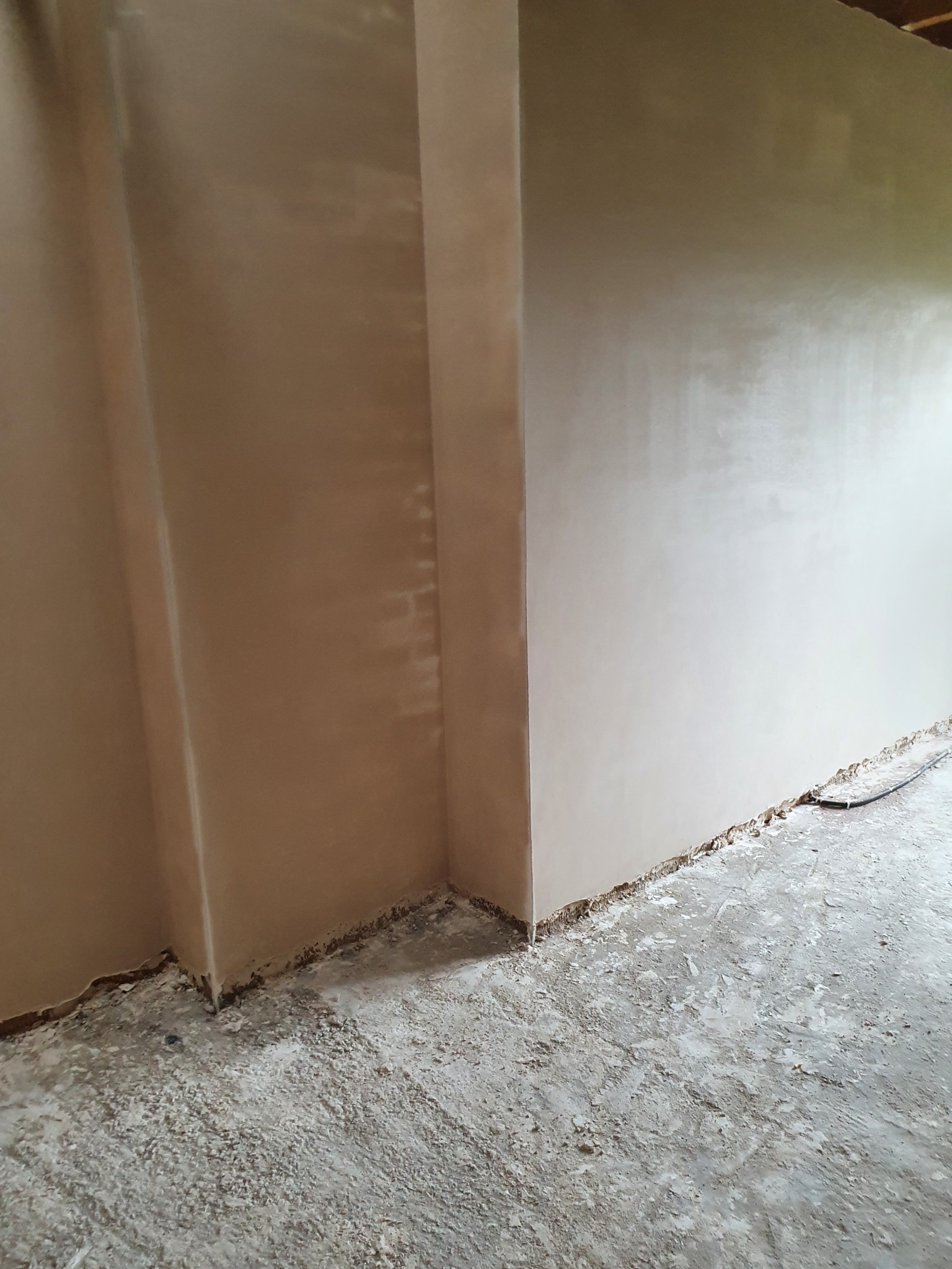 Świeżo nałożone tynki maszynowe na ścianach wewnętrznych, widoczny narożnik i zabrudzony podkład podłogowy.