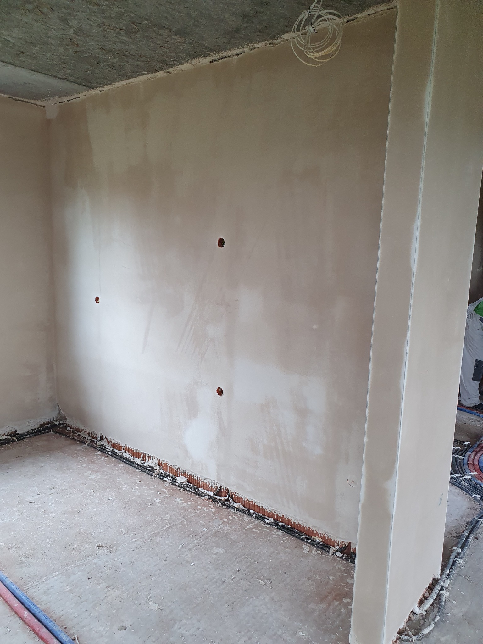 Wnętrze po nałożeniu tynku gipsowego, widoczne otwory na puszki elektryczne, kable przy podłodze i surowy betonowy strop.