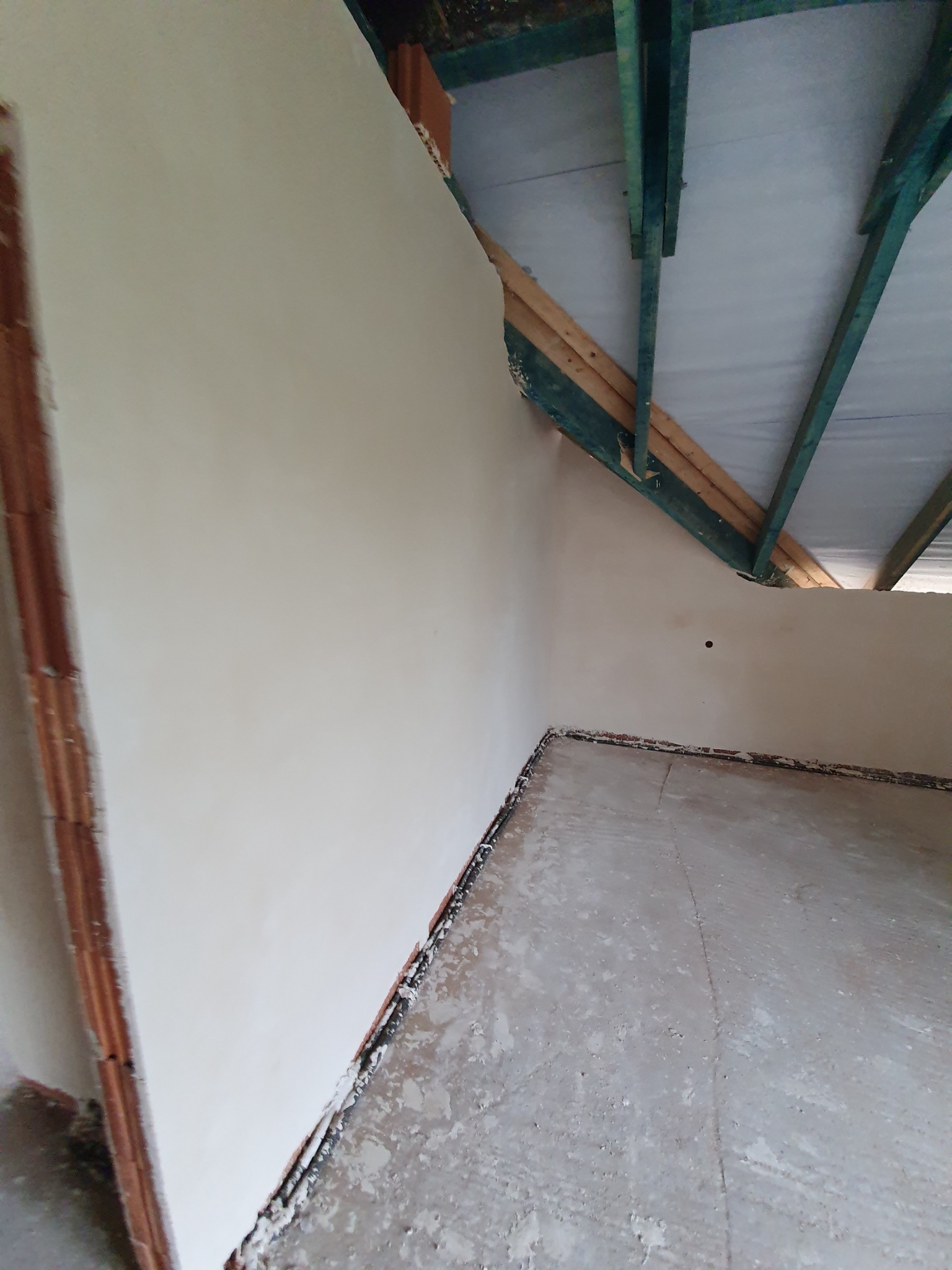 Świeżo otynkowane ściany w pokoju na poddaszu, widoczne drewniane elementy konstrukcji dachu pomalowane na zielono.