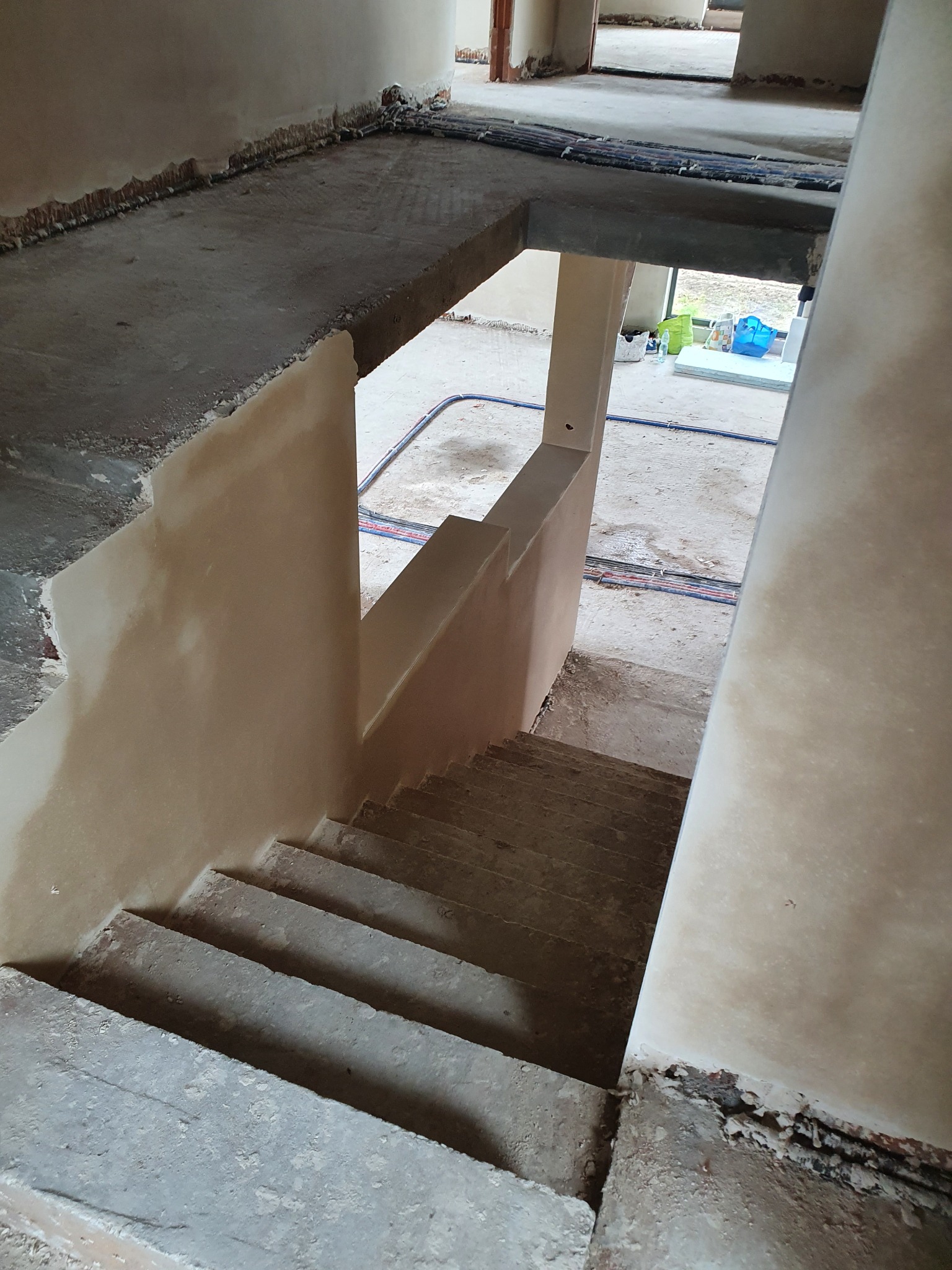 Surowe schody w trakcie prac wykończeniowych, z widocznymi śladami po tynkowaniu na ścianach i przewodami elektrycznymi wzdłuż podłogi.