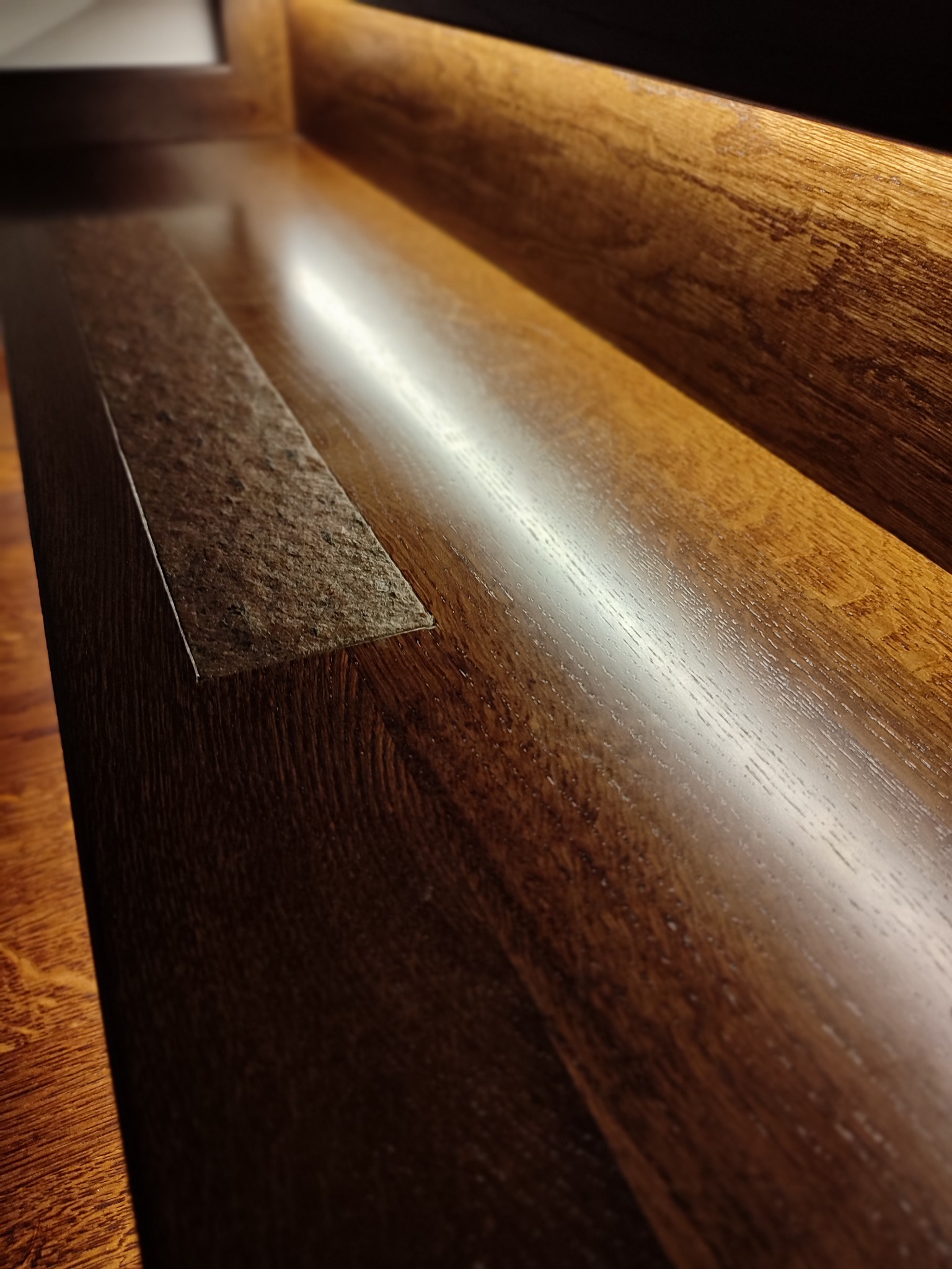 Fragment drewnianych schodów z wbudowanym oświetleniem LED, ukazujący detale tekstury drewna i kontrast materiałów.