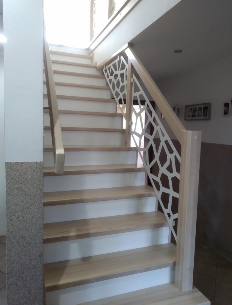 Jasne schody z drewnianymi stopniami i białą podstopnicą, z nowoczesną balustradą o geometrycznym wzorze, widok z dołu.