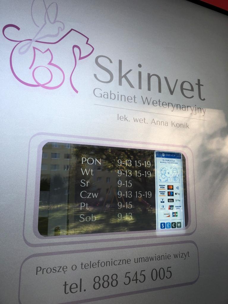 Szyld gabinetu weterynaryjnego Skinvet z godzinami otwarcia i numerem telefonu, widoczny symbol psa i kota w logo.