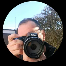 Mężczyzna robiący selfie z aparatem Nikon, widoczne powiadomienie WhatsApp w tle.