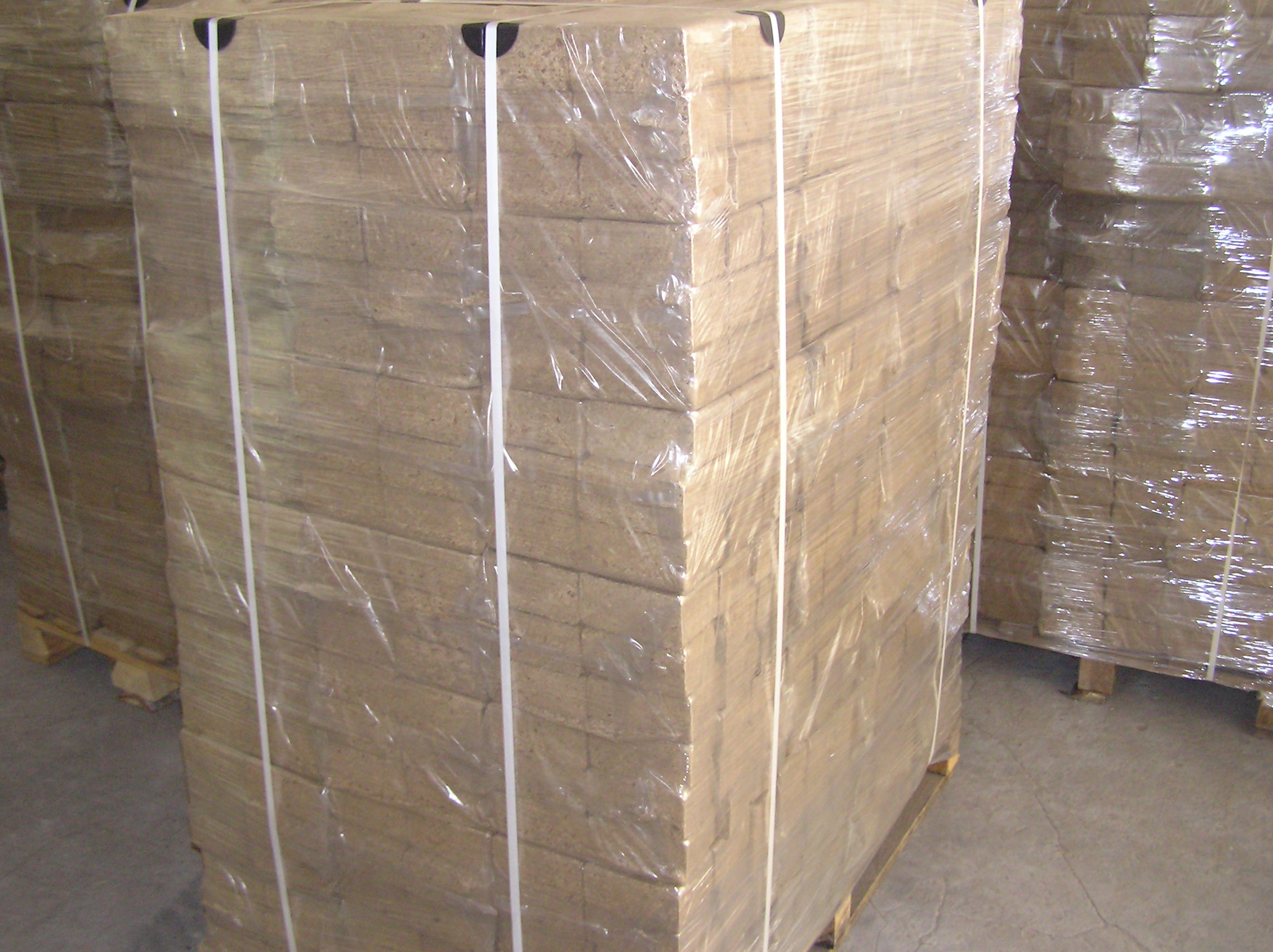Paleta z kostkami sprasowanego materiału opałowego, owinięta folią i zabezpieczona taśmami, widoczna w magazynie.