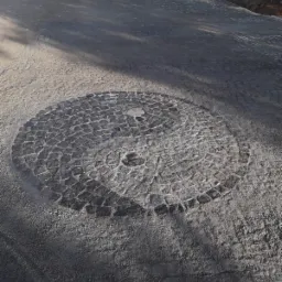 Okrągła mozaika z kostki granitowej w kształcie symbolu Yin i Yang, wkomponowana w nawierzchnię z szarej kostki, widoczna w trakcie prac wykończeniowych.