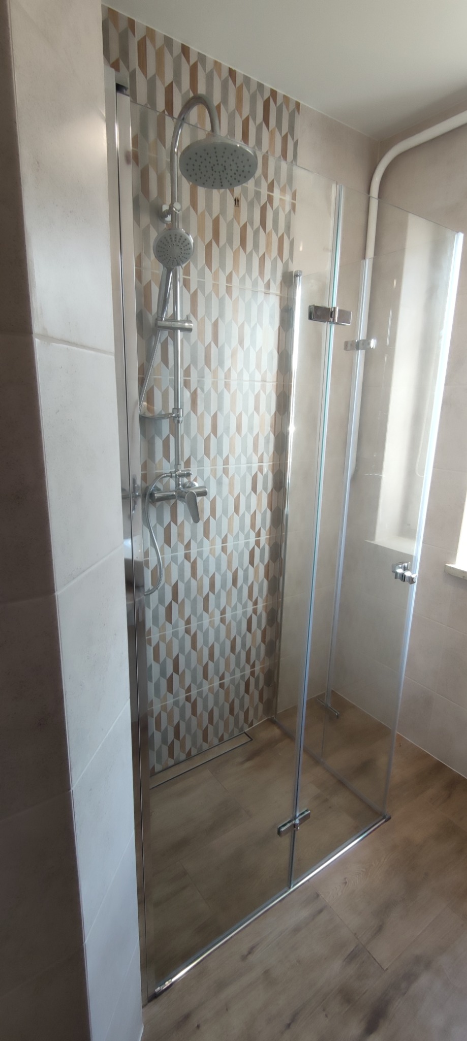 Kabina prysznicowa z geometrycznymi płytkami w Przybówce, widoczne chromowane zawiasy i deszczownica.