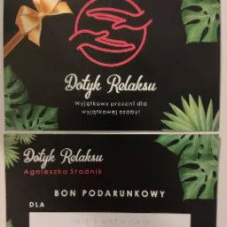 Karta podarunkowa do salonu 'Dotyk Relaksu' z motywem tropikalnych liści, zawierająca logo z dłońmi w okręgu i informację o możliwości umówienia wizyty.