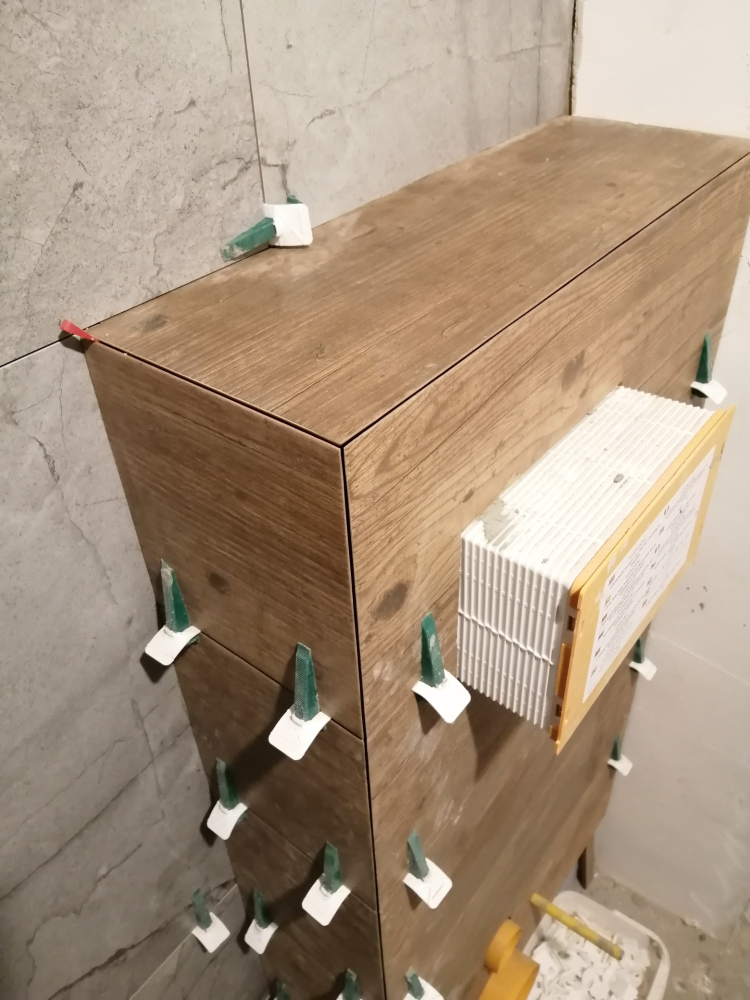 Obudowa stelaża WC z płytek drewnopodobnych, z użyciem klipsów poziomujących, w trakcie prac wykończeniowych łazienki.