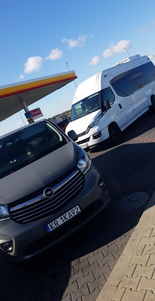 Szary samochód osobowy i biały bus zaparkowane przy stacji benzynowej Shell w słoneczny dzień.