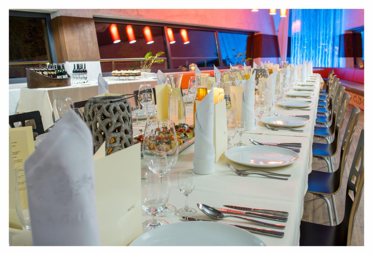 Uroczysty stół bankietowy z białym obrusem, nakryciami, dekoracjami w postaci szklanych naczyń z kompozycjami owocowymi i ażurowych lampionów, przygotowany na imprezę w restauracji z czerwonym...