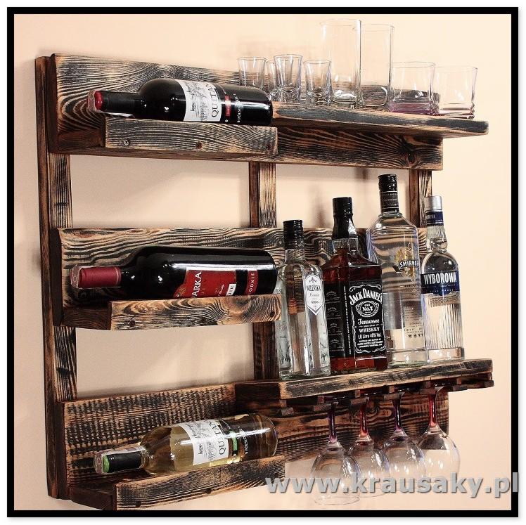 Rustykalny regał na wino i alkohole wykonany z postarzanego drewna, eksponujący butelki wina, wódki, whisky oraz kieliszki, z widocznym logo firmy na dole.