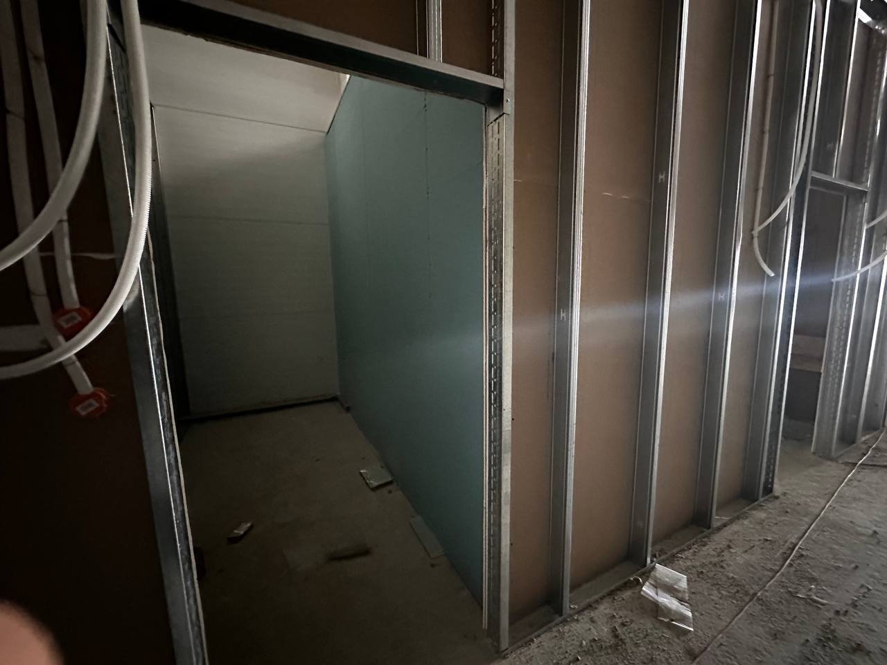 Montaż płyty karton gips na metalowym stelażu, widoczne kable elektryczne. Ściana działowa w trakcie budowy, surowy stan wykończenia wnętrza.