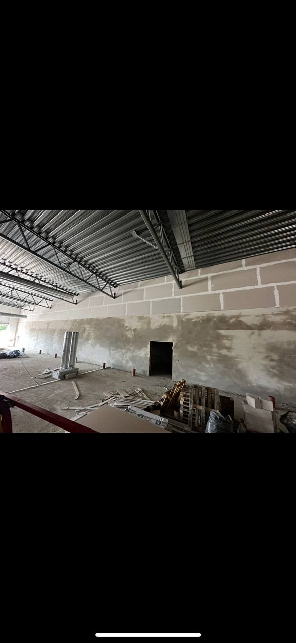 Wnętrze w trakcie prac wykończeniowych: surowa ściana z bloków, częściowo pokryta gładzią, widoczne elementy konstrukcji dachu i porozrzucane materiały budowlane.