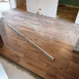 Układanie płytek imitujących drewno w Tarnowie, widoczna poziomica i krzyżyki dystansowe, surowy stan ścian.