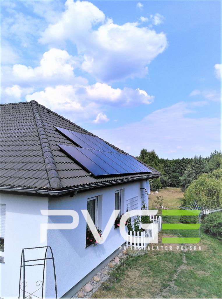 Panele słoneczne na dachu domu jednorodzinnego w Lublinie, widoczne z perspektywy ogrodu w słoneczny dzień.