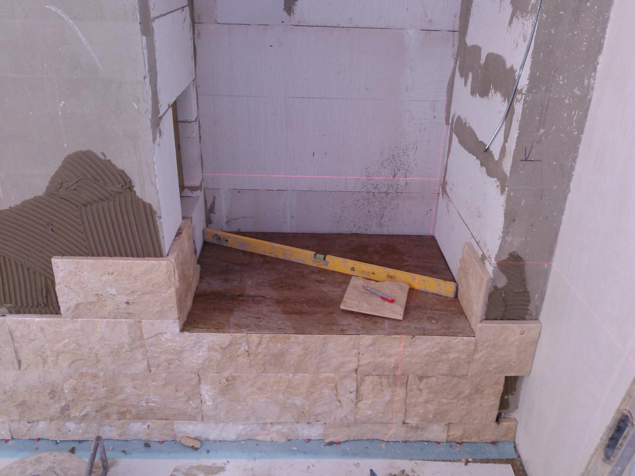 Wnęka w trakcie obkładania beżowymi płytkami imitującymi kamień, widoczny poziomica i czerwona linia lasera wyznaczająca poziom, klej na ścianie przygotowany pod płytki.