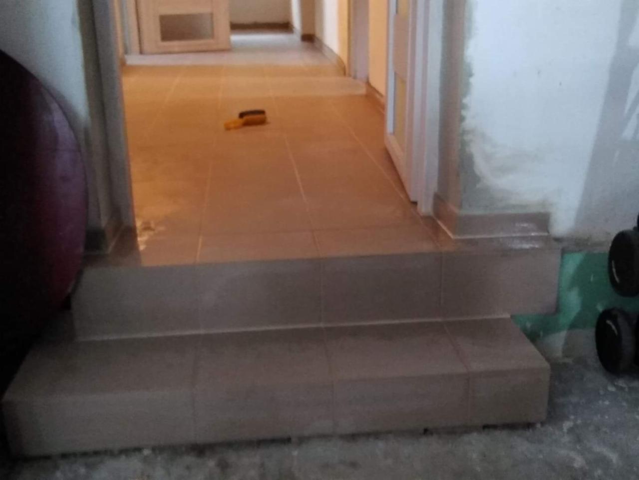 Wykończone schody z płytek ceramicznych wewnątrz budynku, widoczne ślady po fugowaniu na ścianie i podłodze, żółta szpachelka leży na podłodze.