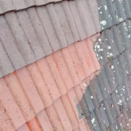 Fragment dachu z dachówki ceramicznej, widoczny obszar po czyszczeniu z mchu i zabrudzeń, kontrastujący z obszarem jeszcze nieczyszczonym, widok z góry.