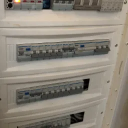 Rozdzielnica elektryczna z widocznymi bezpiecznikami i włącznikami, niektóre z diodami LED sygnalizującymi stan pracy, marki Hager.