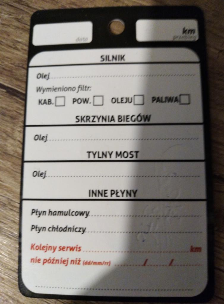 Etykieta serwisowa pojazdu z informacjami o wymianie oleju silnikowego, filtrów (kabiny, powietrza, oleju, paliwa), oleju w skrzyni biegów i tylnym moście, płynu hamulcowego oraz chłodniczego.