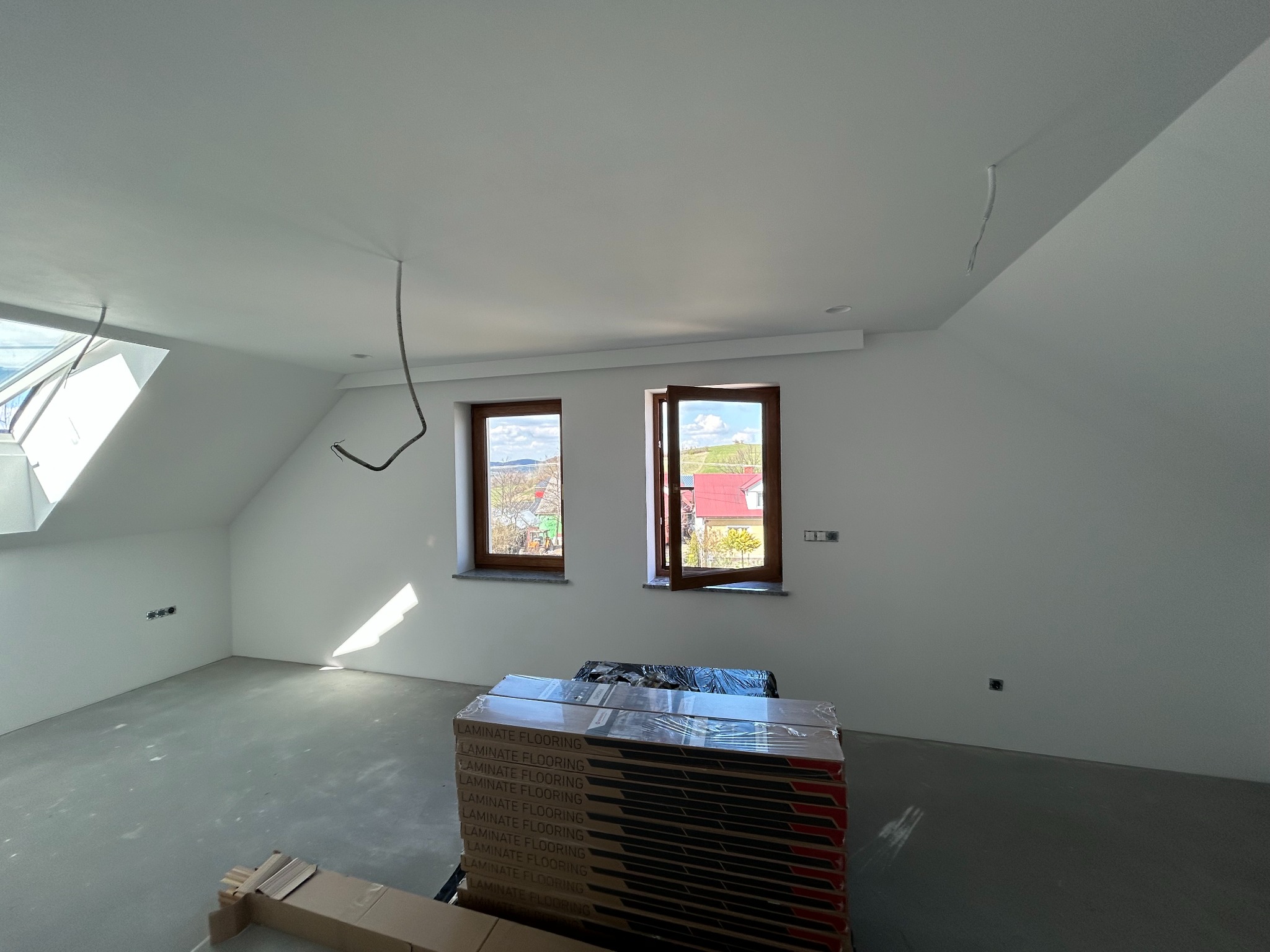 Poddasze po gładziowaniu ścian i wylewce, przygotowane do montażu paneli podłogowych. Widoczne okna dachowe i pakiety paneli.