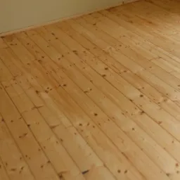 Jasne, lakierowane deski parkietowe ułożone pod kątem, widoczne sęki i naturalny wzór drewna, ściana w tle w neutralnym odcieniu.