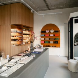 Koral i Kapi Usługi Stolarskie S.C Rafał Koralewski Błażej Błaszczyk - Wnętrze sklepu z drewnianą zabudową, półkami podświetlanymi LED, ekspozycją biżuterii na ladzie i torebkami na pomarańczowych półkach na ścianie.